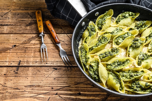 Coquilles de pâtes Conchiglioni farcies aux épinards et fromage cuit au four avec sauce dans une casserole sur table en bois. Vue de dessus.