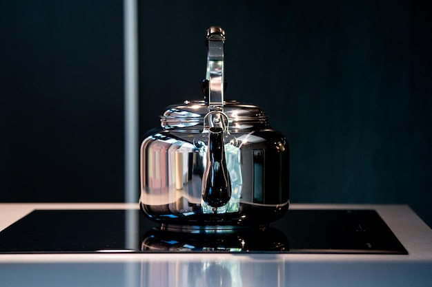 Photo corbeau d'eau en acier inoxydable ou théière vintage kettle sur cuisinière électronique sur fond bleu foncé moderne