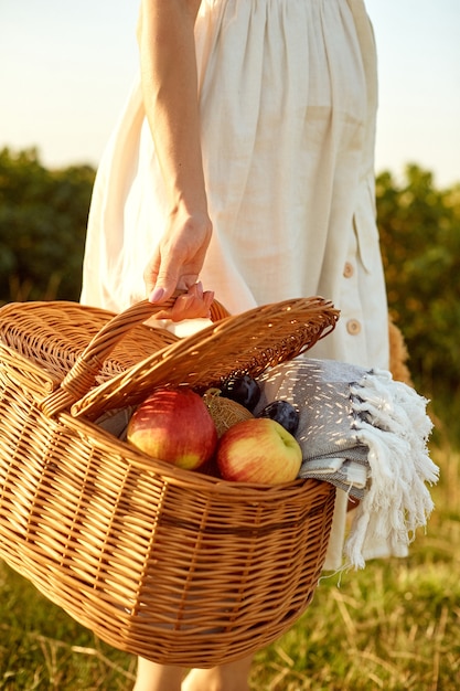 Corbeille de fruits en osier entre les mains d'une femme.