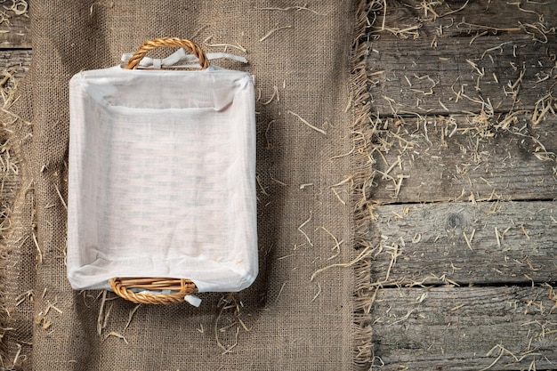 Photo corbeille à pain en osier vide avec serviette blanche sur toile de jute recouverte de paille ou de foin de style champêtre rustique voir ci-dessus