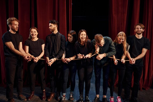 Avec une corde dans les mains Groupe d'acteurs en vêtements de couleur sombre en répétition au théâtre