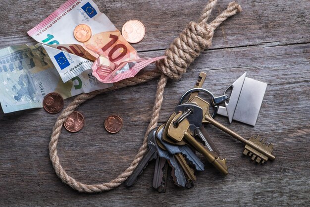 Corde du pendu avec clés de maison et argent sur une surface en bois marron