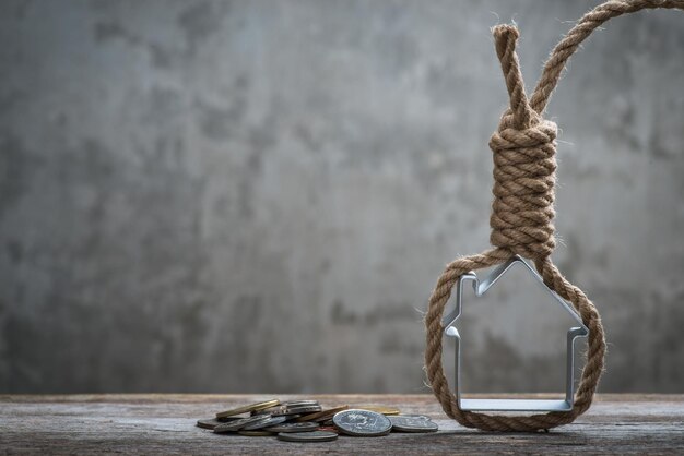 Corde du pendu avec maison et argent sur une surface en bois marron