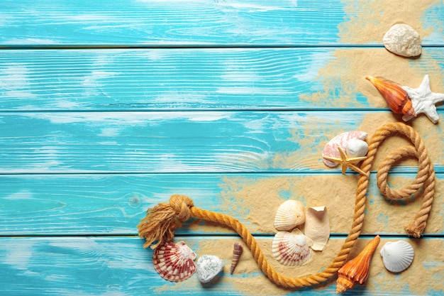 Photo corde de mer avec de nombreux coquillages sur le sable de la mer sur un fond en bois bleu