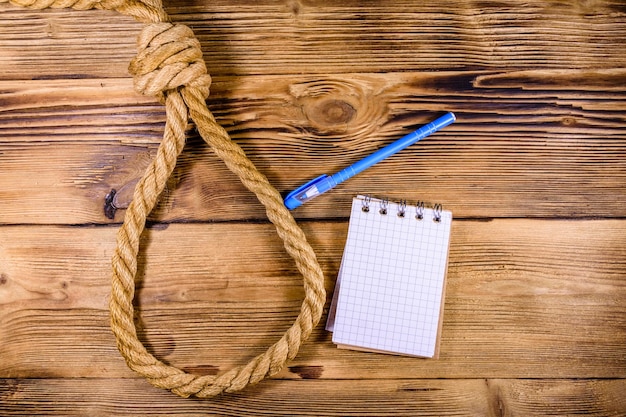 Photo corde avec nœud coulant pour le bloc-notes vierge suicide et stylo sur fond de bois