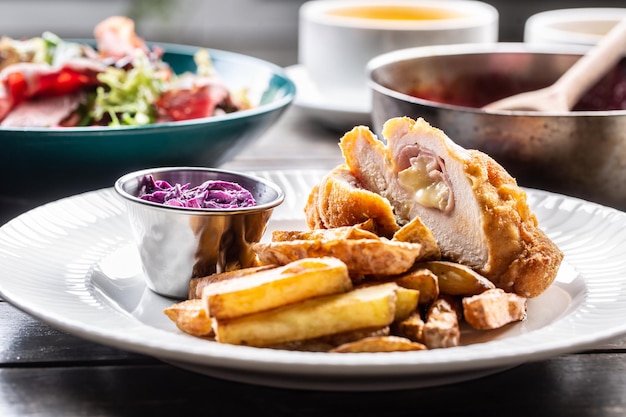 Cordon bleu de poulet avec du jambon et du fromage à l'intérieur servi avec des quartiers de pommes de terre frites et une salade de chou rouge.