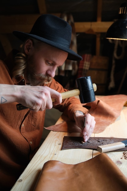 Photo cordonnier se concentrant sur son travail à table, il travaille avec du textile en cuir et un marteau dans un atelier