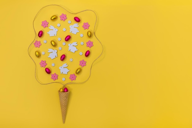 Corne de gaufre à la crème glacée avec décoration de Pâques fleurs en bois lapins et oeufs sur fond jaune