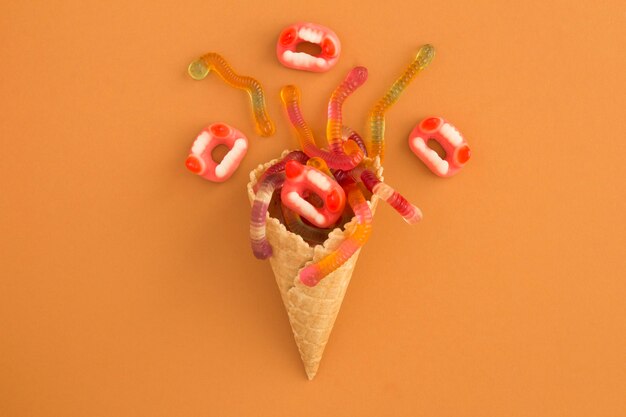 Photo cornet de crème glacée avec des bonbons pour halloween sur une surface orange. vue de dessus. espace de copie.