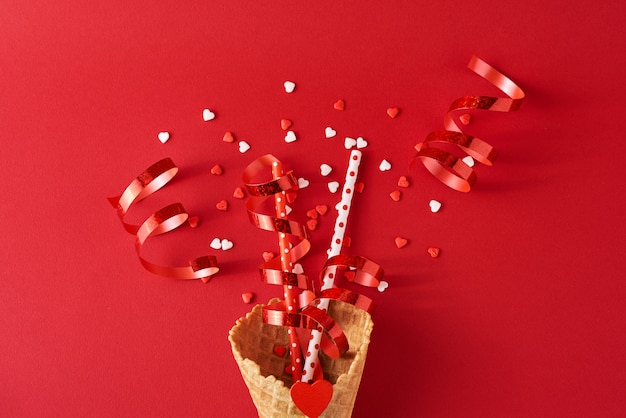 Cornet de crème glacée festive avec des décorations et des confettis sur backgrond rouge, vue de dessus à plat. Concept de minimalisme créatif