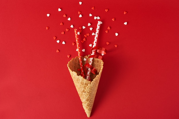 Cornet de crème glacée festive avec décorations et confettis sur fond rouge, vue de dessus à plat. Concept de minimalisme créatif