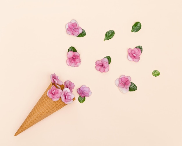 Cornet de crème glacée gaufré avec de petites fleurs roses et des feuilles vertes composition minimale à plat d'été