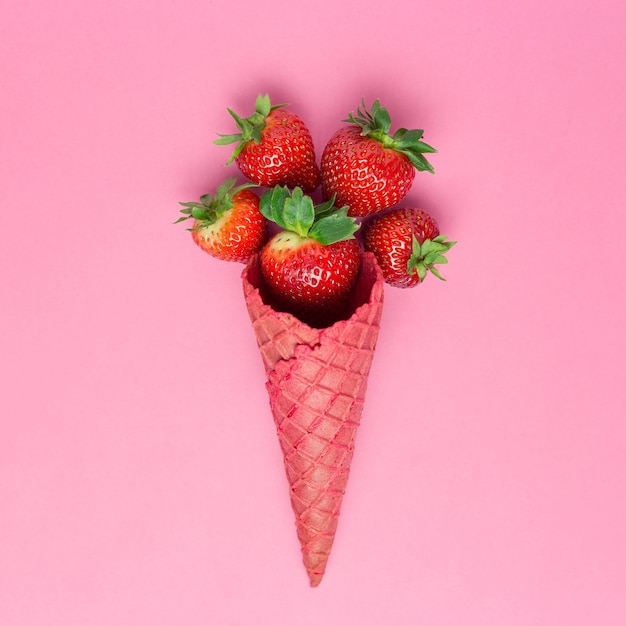 Cornet de crème glacée rose avec des fraises fraîches sur une surface rose pastel. Composition laïque plate d'été minimale. Concept de fabrication de crème glacée maison. Copier l'espace, carré