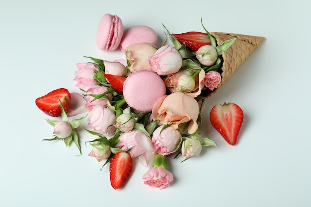 Cornet gaufré avec fleurs, fraises et macarons sur fond blanc
