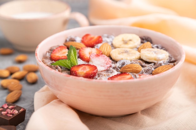 Cornflakes au chocolat avec lait, fraise et amandes dans un bol en céramique sur fond de béton gris et textile en lin orange. Vue latérale, gros plan, mise au point sélective.