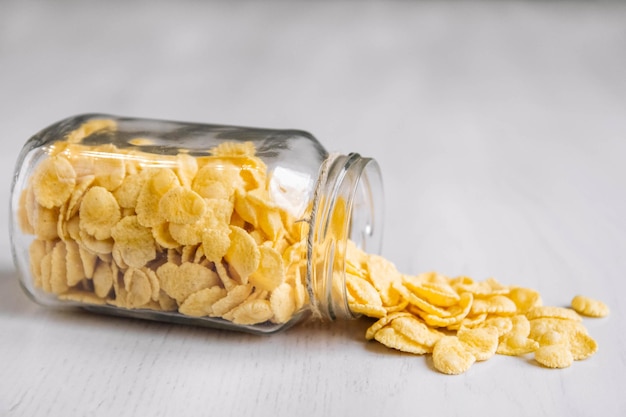 Cornflakes dans un bocal en verre sur une surface en bois blanche. Place pour votre texte