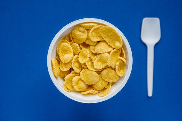 Cornflakes dans un bol blanc avec cuillère sur fond bleu. Vue de dessus. Copie, espace vide pour le texte