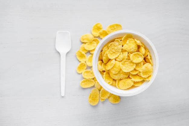 Cornflakes Dans Un Bol Blanc Avec Cuillère Sur Fond De Bois Blanc. Vue De Dessus. Copie, Espace Vide Pour Le Texte