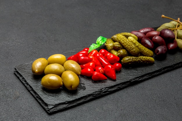 Cornichons mélangés sur planche de service. Olives, câpres et poivrons