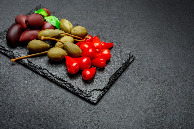 Cornichons mixtes sur planche de service en pierre. Olives, câpres et poivrons