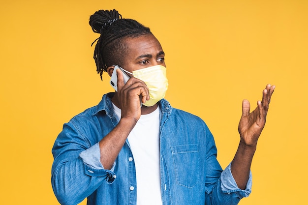 Coronavirus. Homme noir afro-américain portant un masque hygiénique pour prévenir les infections, les maladies respiratoires aéroportées telles que la grippe, 2019-nCoV. Isolé sur fond jaune. Utiliser le téléphone