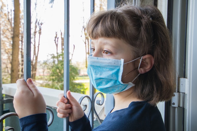 Coronavirus Jeune fille en isolement à la maison mise en quarantaine automatique portant un masque protecteur pour la propagation du virus de la maladie en regardant par les fenêtres
