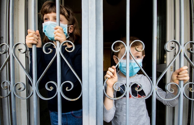 Coronavirus Jeunes enfants à la maison isolement de la quarantaine automatique portant un masque protecteur pour la propagation du virus de la maladie en regardant par les fenêtres