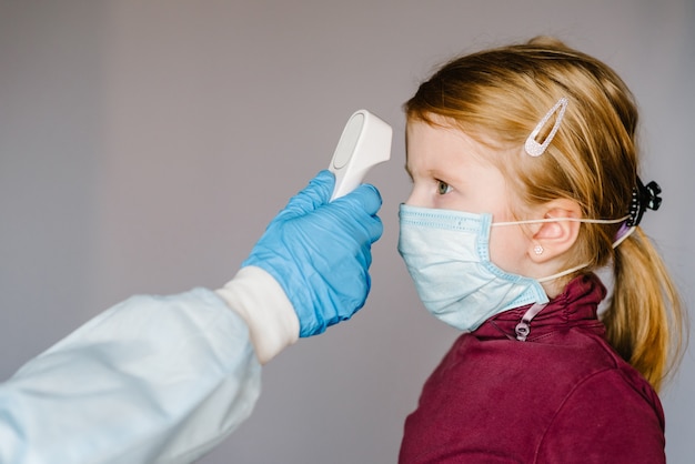 Coronavirus. Médecin vérifie la température corporelle de la jeune fille à l'aide d'un thermomètre frontal infrarouge (pistolet) pour détecter les symptômes du virus - concept d'épidémie épidémique. Haute température.