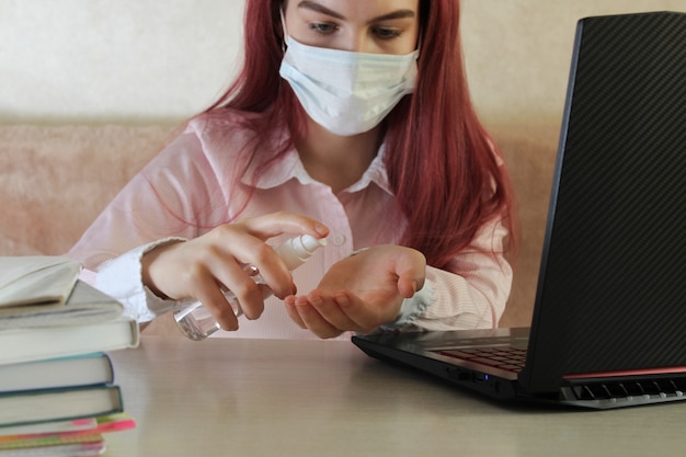 Photo coronavirus. quarantaine. formation en ligne et travail indépendant. ordinateur portable et fille nettoyer ses mains avec du gel désinfectant. pandémie de coronavirus dans le monde.