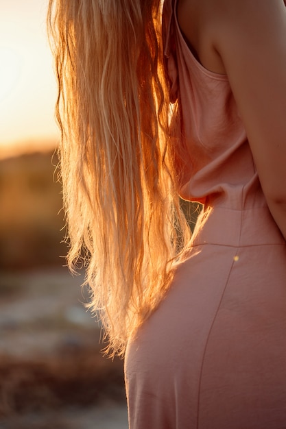 Corps de la belle jeune femme blonde caucasienne en robe rose dans un champ désert au coucher du soleil