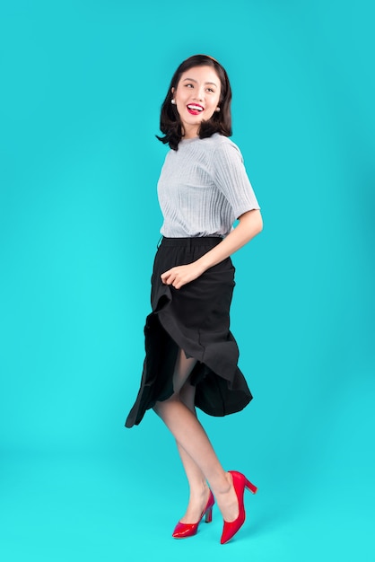 Corps entier de femme asiatique souriante vêtue d'une robe de style pin-up sur bleu.