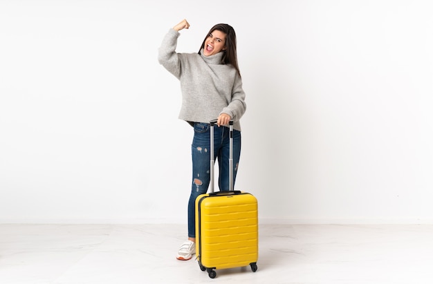 Un corps entier d'une femme voyageur avec une valise sur un mur blanc isolé célébrant une victoire