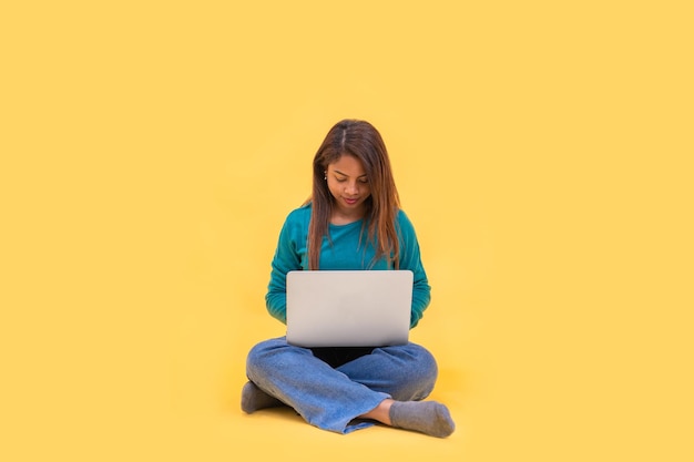 Corps entier jeune femme latine s sur le travail au sol sur ordinateur portable isolé sur fond jaune studio