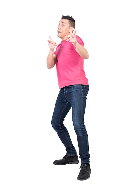 Corps entier de jeune modèle masculin drôle avec des cheveux noirs en t-shirt rose et un jean regardant et pointant vers la caméra sur fond blanc