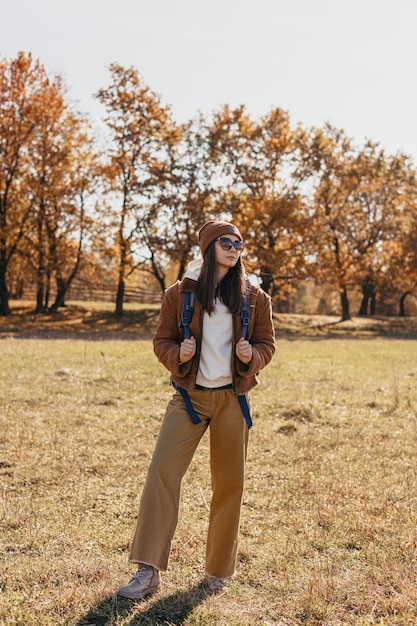 Corps entier de routard féminin debout sur l'herbe dans les bois d'automne par temps ensoleillé