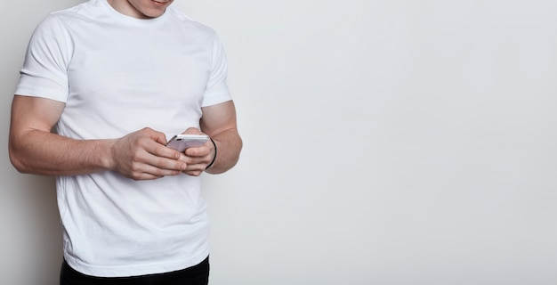 Un corps de garçon musclé portant un T-shirt blanc tenant un smartphone en tapant un message communiquant avec des personnes en ligne