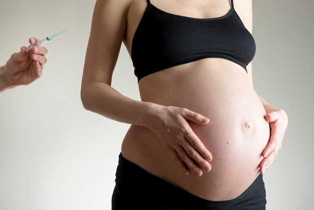 Corps de jeune femme enceinte tenant les mains sur le ventre nu et une main avec une seringue