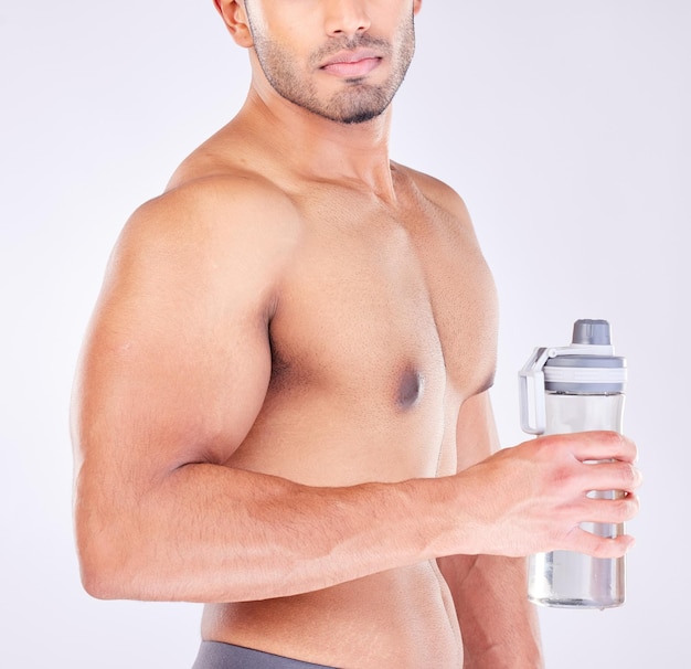 Corps musculaire et homme avec une bouteille d'eau pour l'exercice de soins de santé ou un entraîneur personnel Entraînement de modèle de bien-être ou motivation de force de fitness et entraînement avec des mains fortes sur fond de studio gris
