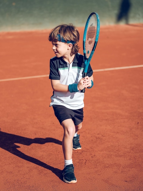 Le corps plein d'un adorable garçon préadolescent concentré en vêtements de sport se préparant à un coup avec une raquette tout en jouant à un match de tennis sur un terrain dur