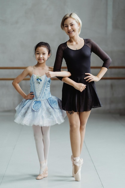 Le corps plein d'enseignant asiatique en pointes debout avec une fille en tutu debout dans le studio de ballet avec