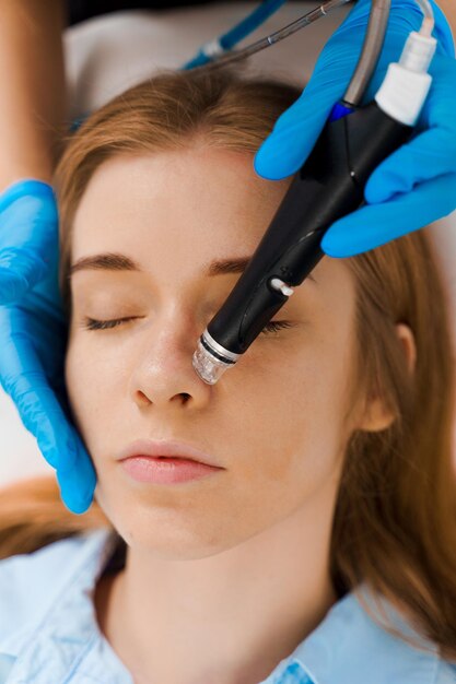 Cosméticienne effectuant un soin du visage HydraPurification faciale du visage pour une femme Purification du visage sans douleur dans la clinique Procédure de purification hydrafaciale avec un dispositif médical dans un centre de beauté