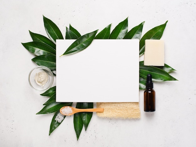 Cosmétique biologique naturelle et brosse de bain mise à plat avec des feuilles sur fond blanc