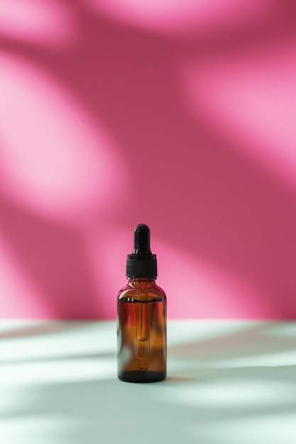 Cosmétique nature en bouteille de verre et ombre sur fond rose Concept de spa de soins du visage et du corps Sérum d'huile d'acide hyaluronique avec collagène et peptides produit de soin de la peau