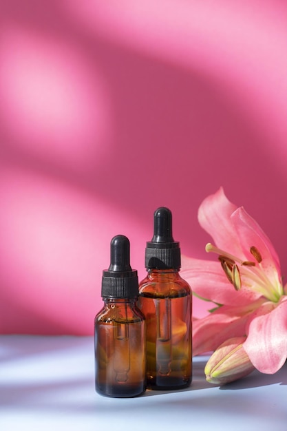 Cosmétique nature dans des bouteilles en verre avec fleur de lys et ombre sur fond rose Concept de spa de soins du visage et du corps Sérum d'huile d'acide hyaluronique avec collagène et peptides produit de soin de la peau