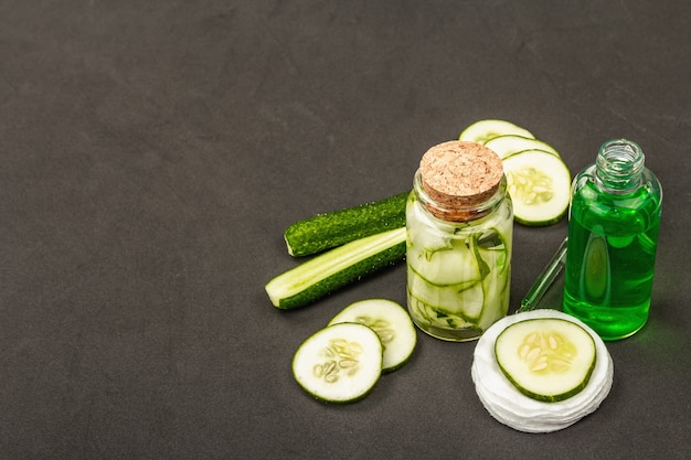 Cosmétiques de concombre faits maison. Masques végétaux détoxifiants pour la peau. Lait visage naturel ou eau tonique. Fond noir mat, espace de copie