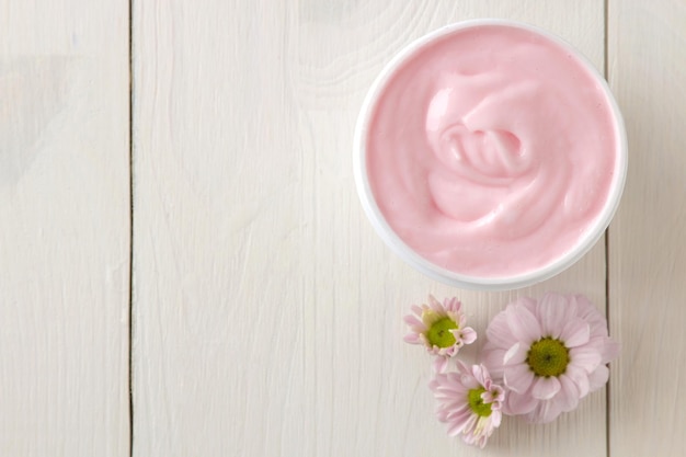 Cosmétiques crème pour le visage et le corps Crème rose et fleur dans un pot blanc sur une vue de dessus de table en bois blanc