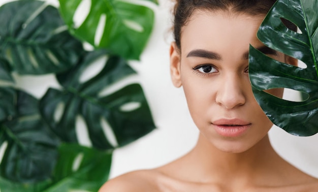 Cosmétiques naturels. Femme afro-américaine contre les feuilles tropicales, panorama