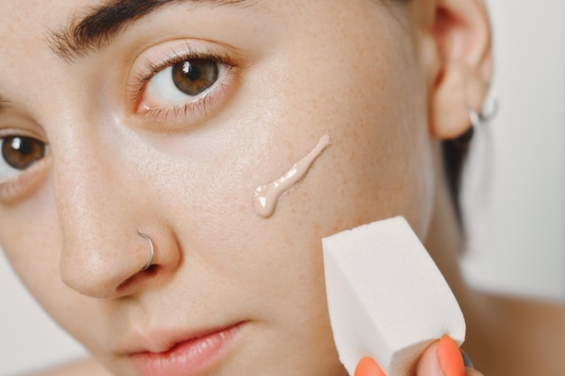 Photo cosmétiques pour l'acné, une femme applique un fond de teint tonal avec une éponge pour masquer les problèmes