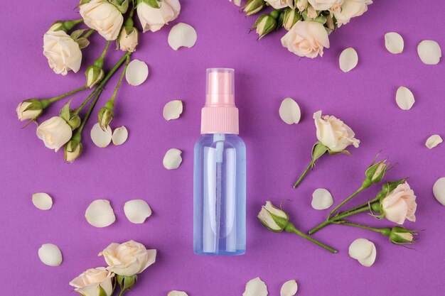 Cosmétiques pour le visage et le corps dans des bouteilles roses avec des roses fraîches sur fond violet vif. spa. vue de dessus