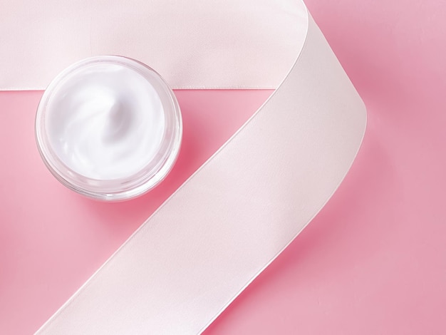 Cosmétiques de soins de la peau pot de crème hydratante pour le visage et ruban de soie blanche sur fond rose produit de beauté gros plan flatlay